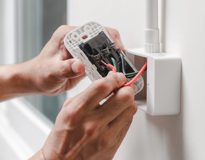 The electrician plugs the power cord into the wall outlet.